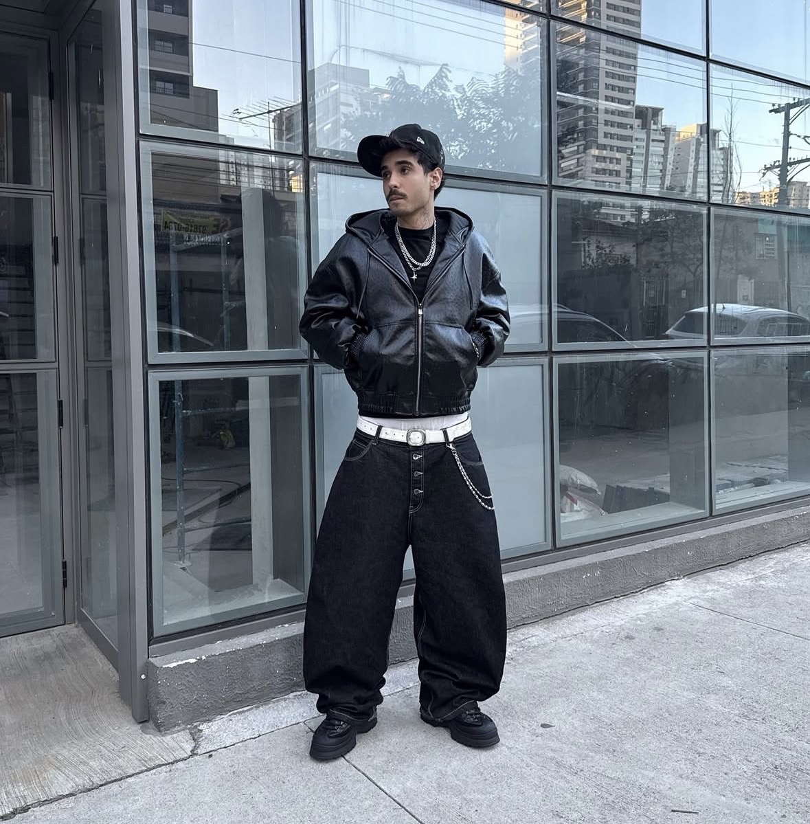Gabriel Satiro com outfit streetwear all black: boné, jaqueta de couro e calça baggy
